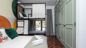 A bunk bed room with a view to the outside, a wooden floor, and a green wardrobe.