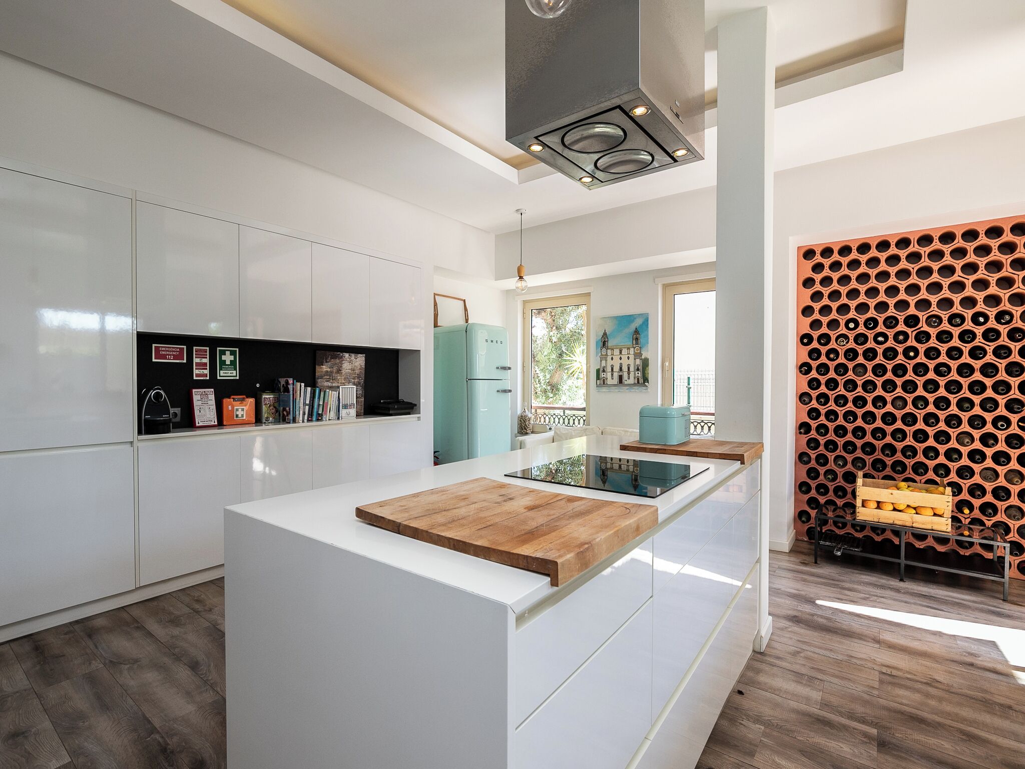 Una cocina moderna con armarios blancos, una isla central con encimera de madera, estufa integrada y una estantería para vinos en la pared.