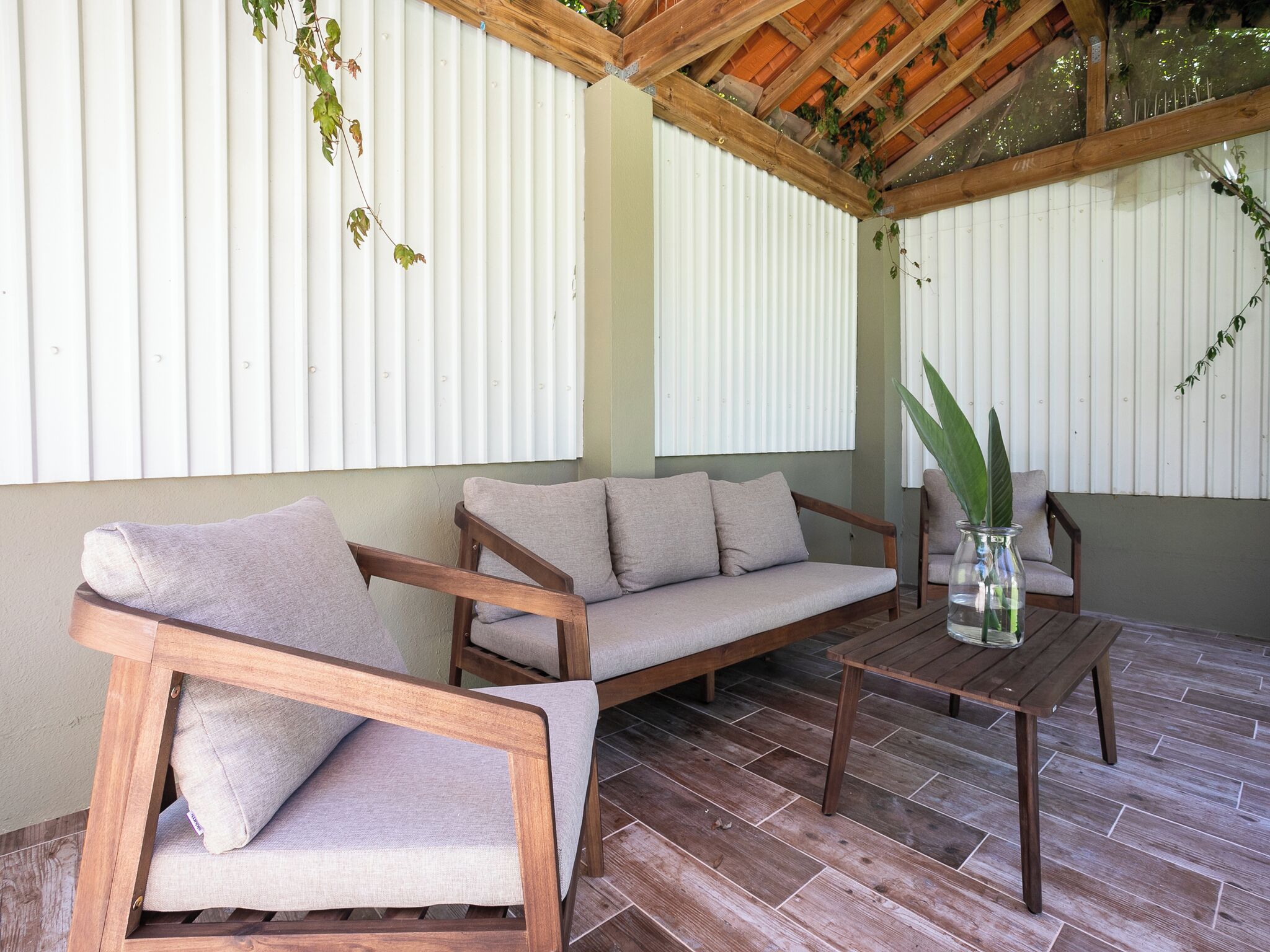 Een overdekt terras met een houten bank, een bank en een tafel.