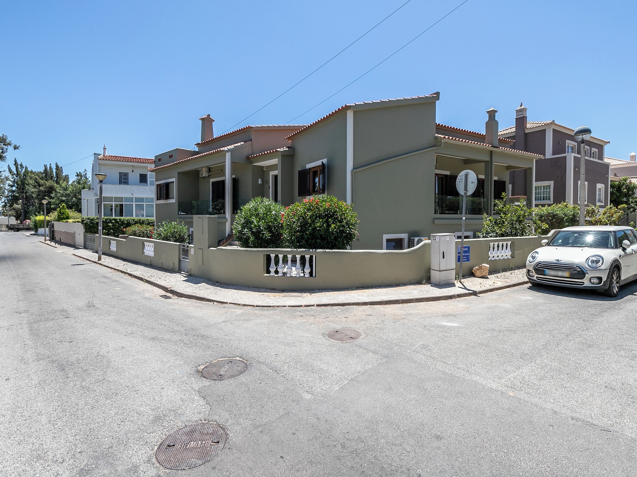 Una calle residencial con casas, un coche estacionado y una tapa de alcantarilla.