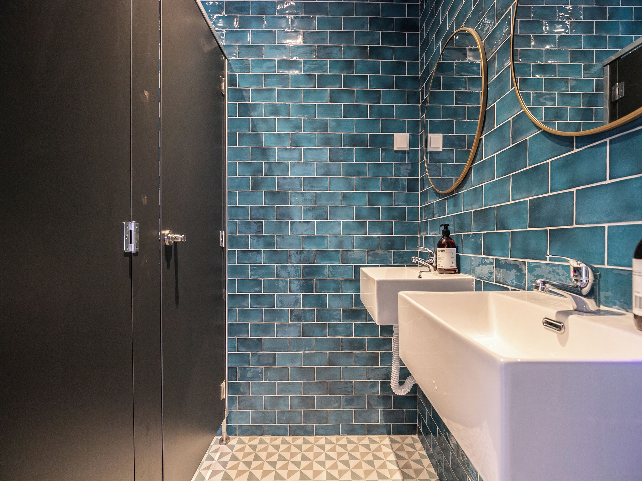 A bathroom with blue-tiled walls, two sinks, and a door.
