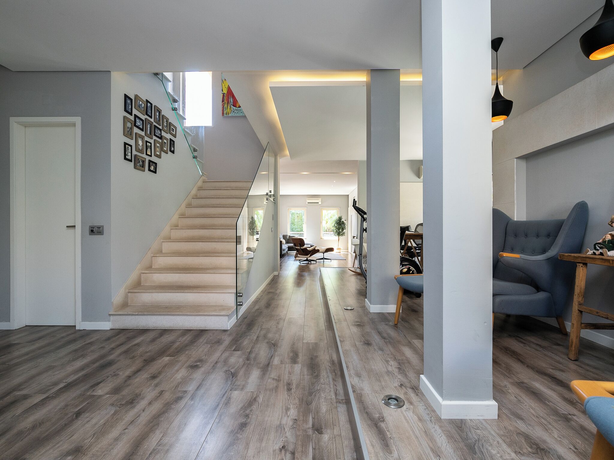 A modern interior with a wooden staircase, a living area with a blue sofa, and a dining area with a table and chairs.