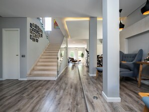 Un interior moderno con una escalera de madera, una sala de estar con un sofá azul y un comedor con mesa y sillas.