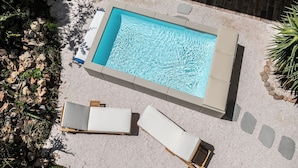 Une piscine rectangulaire à l’eau d’un bleu limpide, entourée d’une terrasse en pierre. On y trouve deux chaises longues avec des coussins blancs.