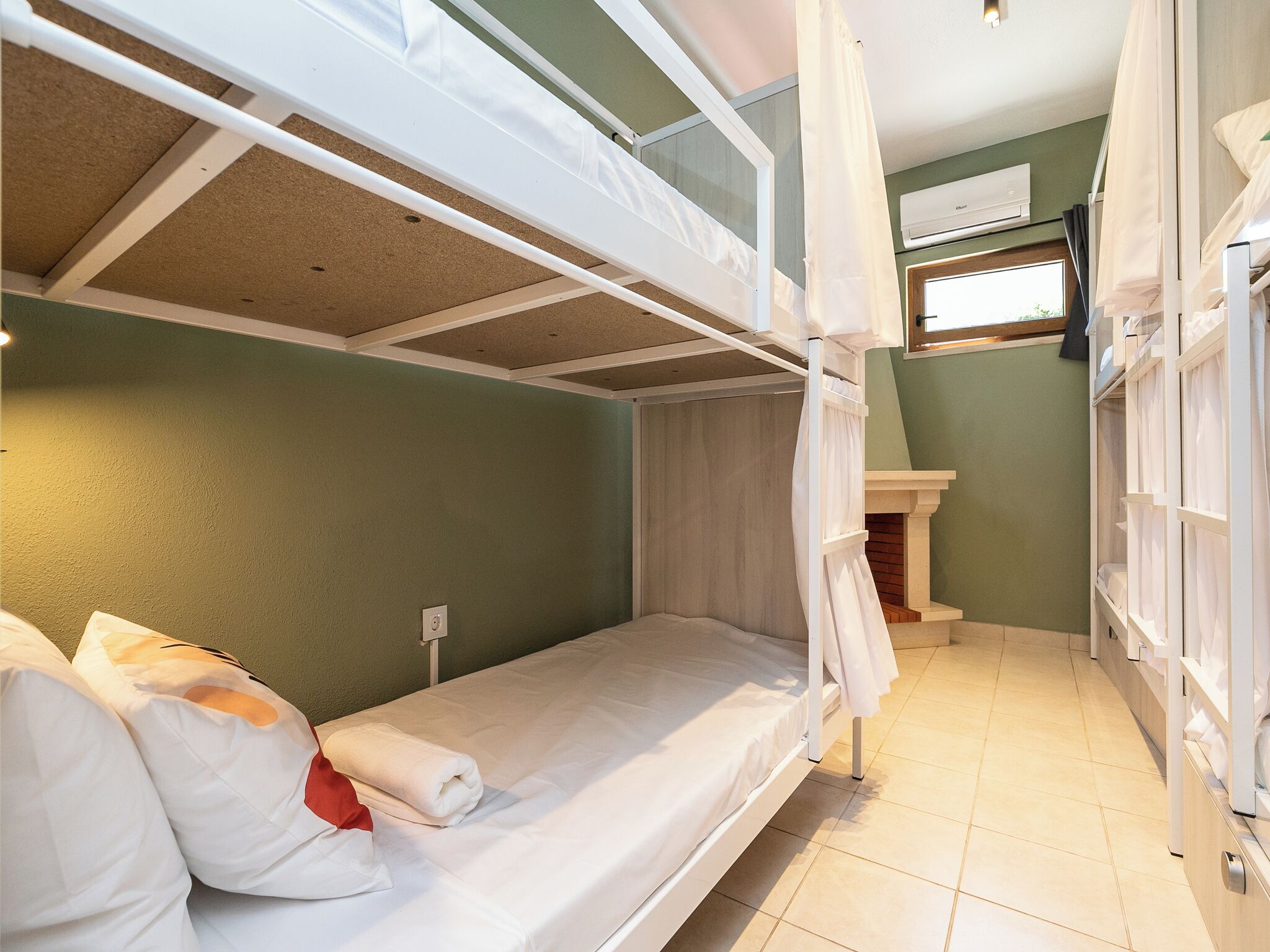 Een slaapkamer met stapelbed, raam, wastafel en een handdoek op het bed.