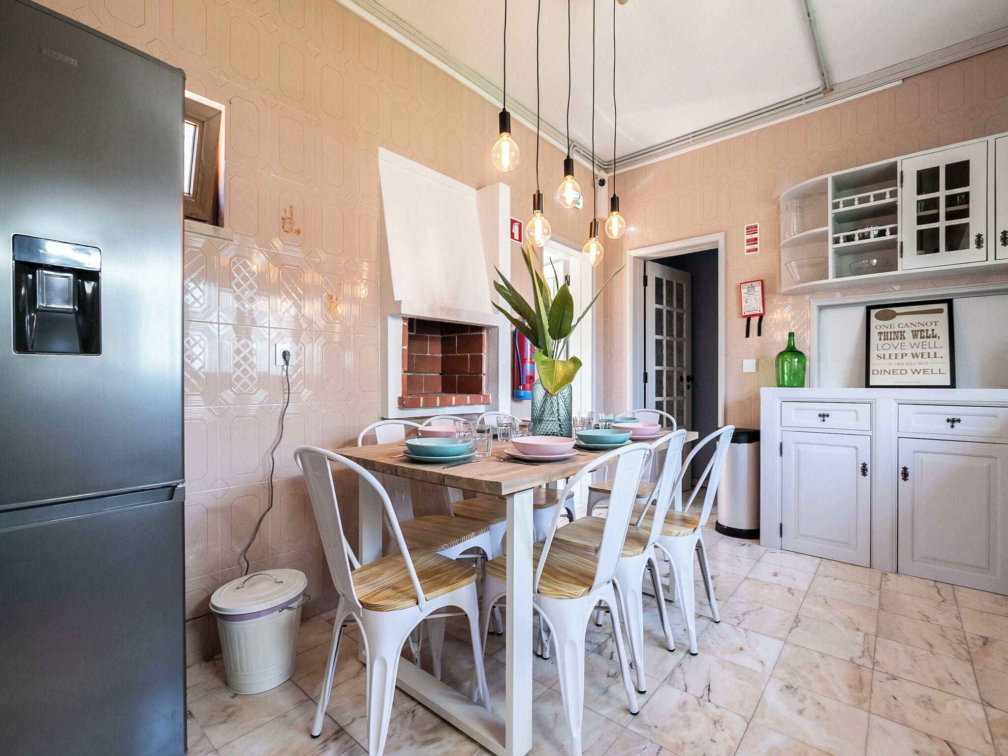 Una cocina moderna con refrigerador empotrado, armarios blancos y una zona de comedor con mesa de madera y sillas blancas.