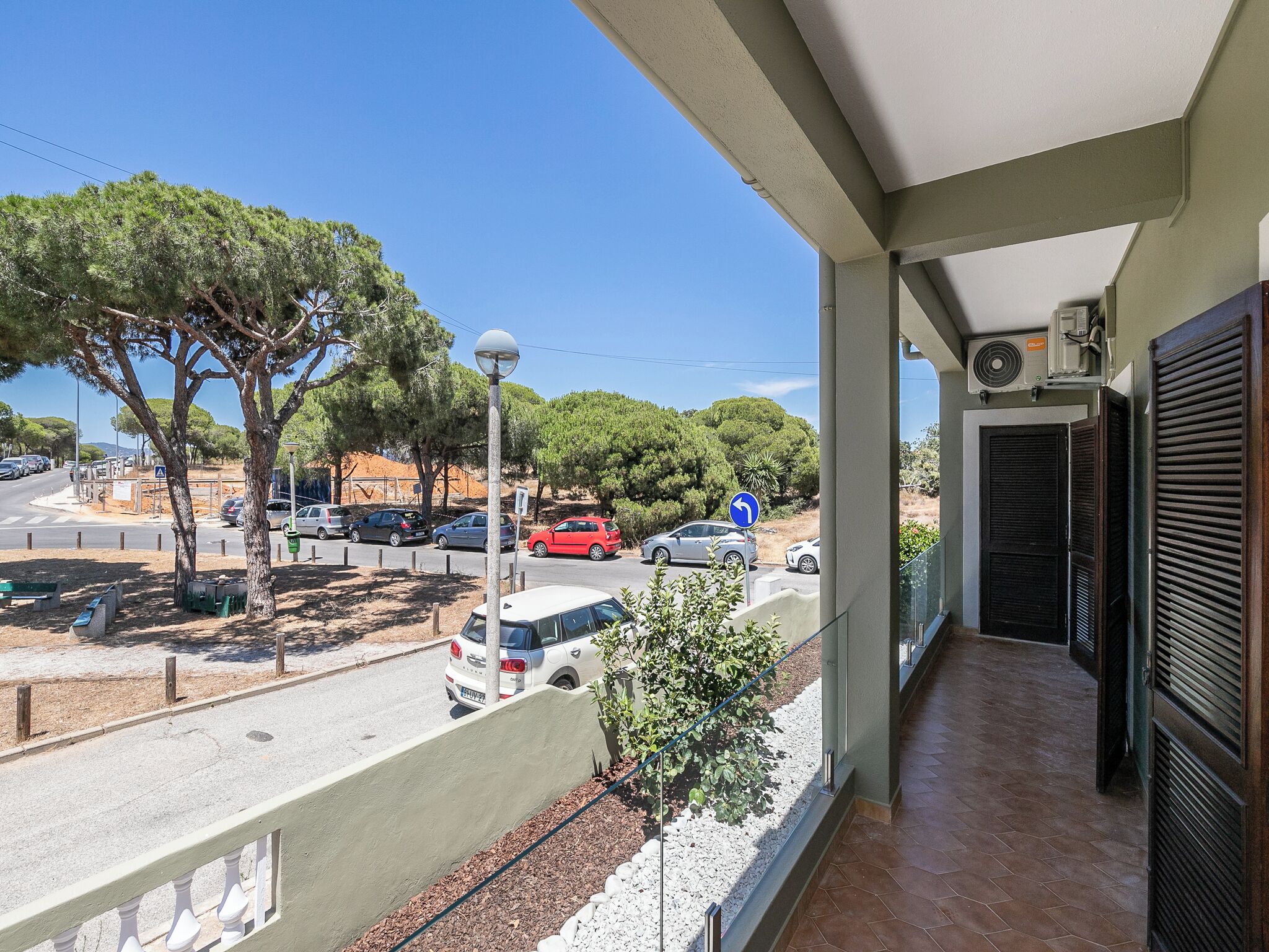 Un balcon donnant sur une rue, des arbres et des voitures garées.