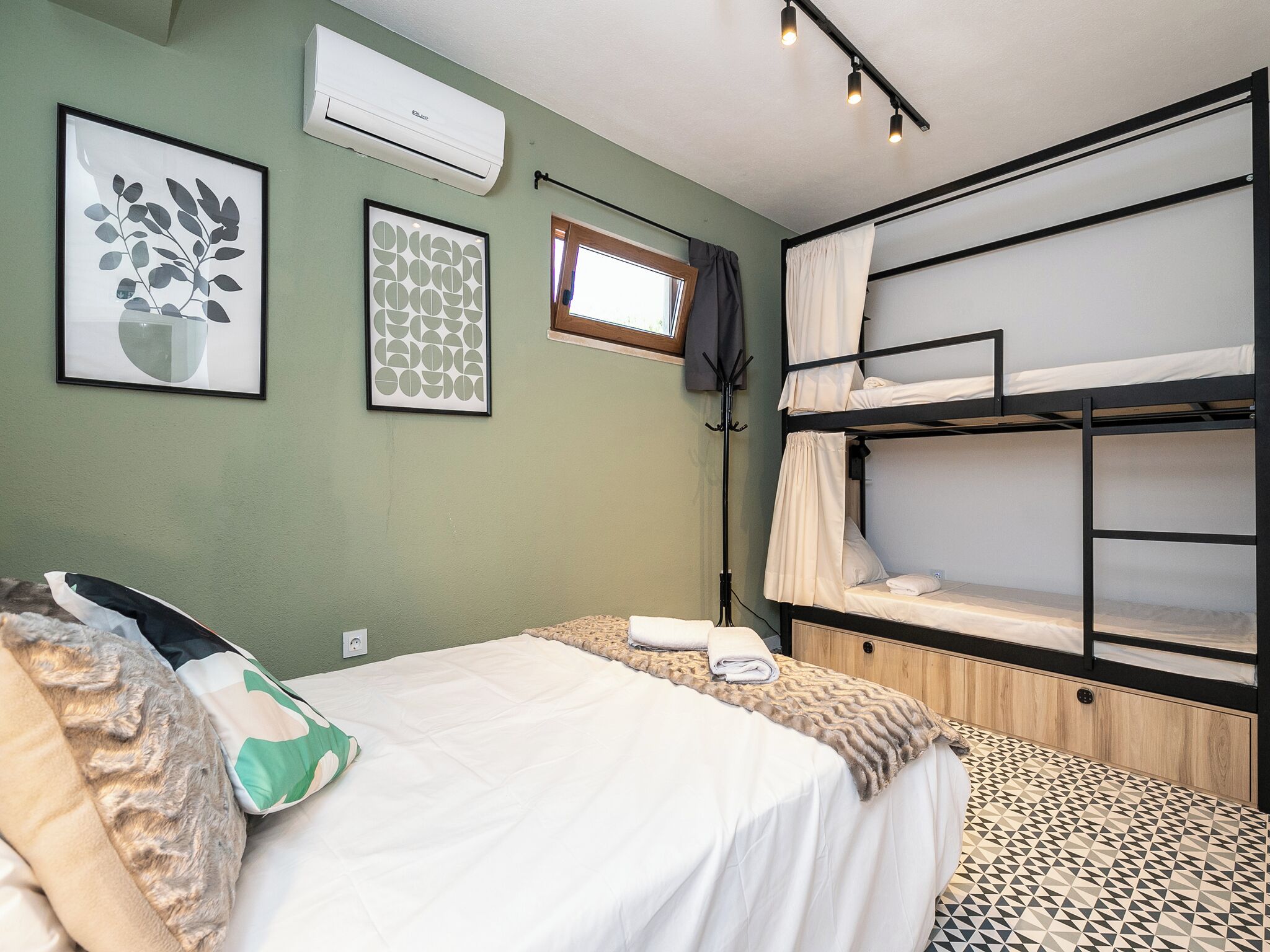 A room with bunk beds, a bed with pillows, a framed plant, and an air conditioner.