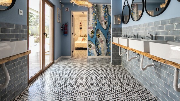 Une salle de bain avec un sol carrelé aux motifs géométriques, un grand miroir et un lavabo fixé au mur.