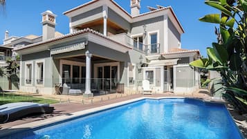 Una casa de dos pisos con piscina, ventanas amplias y un balcón.