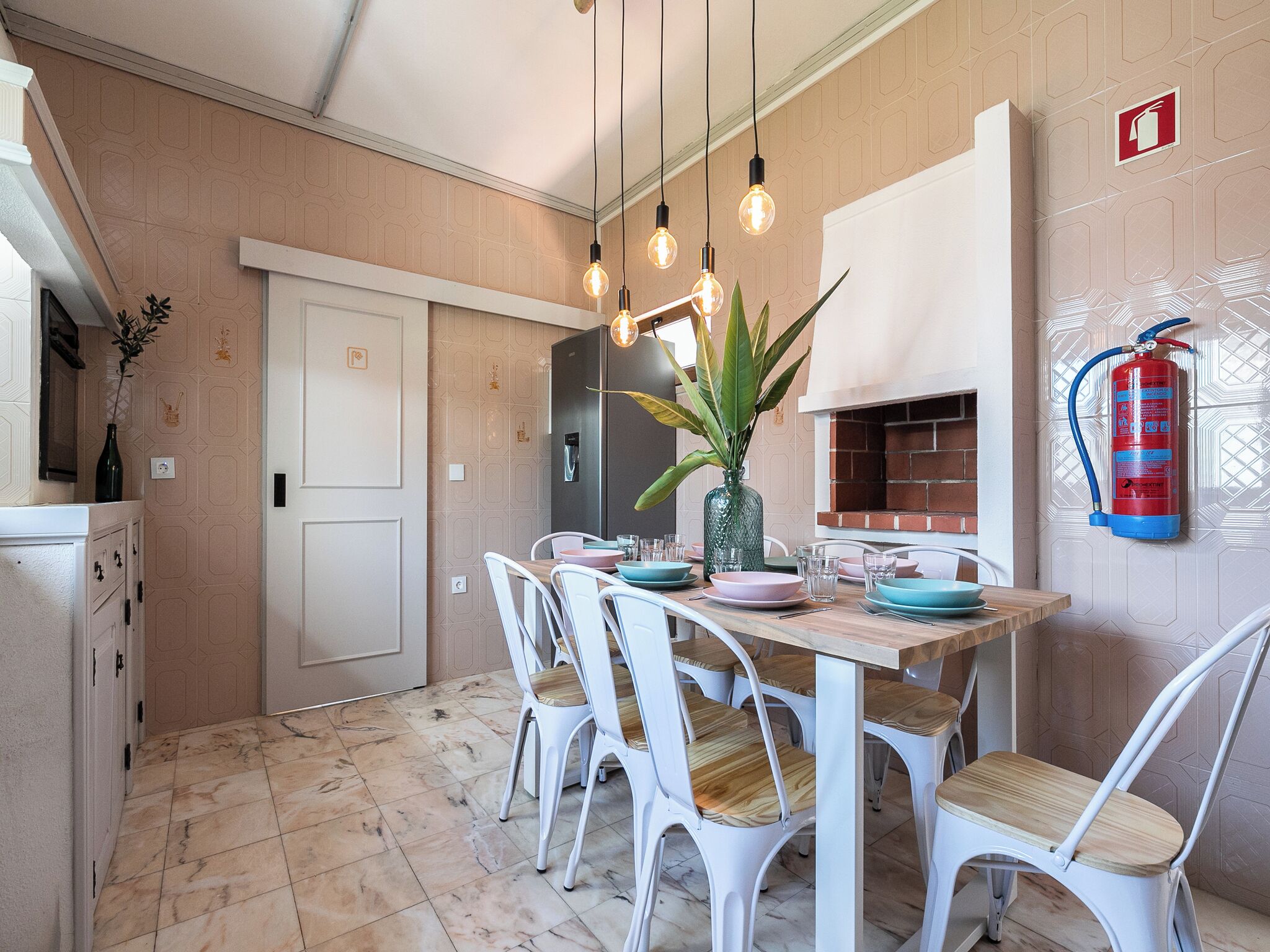 A dining area with a wooden table, white chairs, and hanging light bulbs.