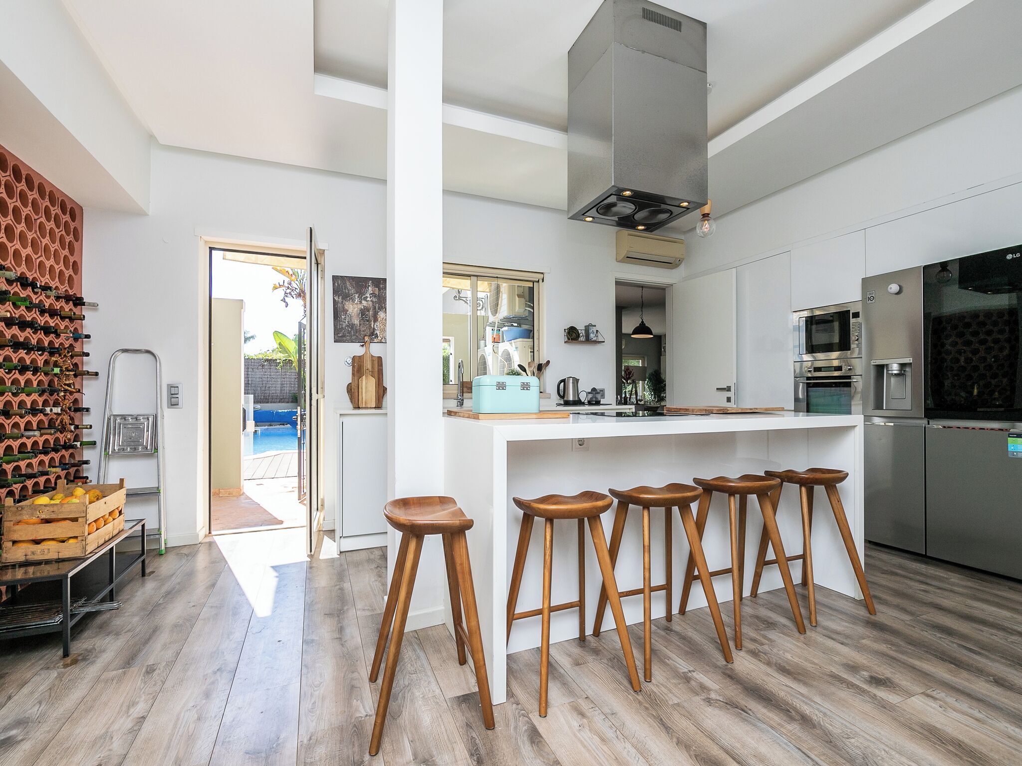 A modern kitchen with a central island, bar stools, stainless steel appliances, and a wine rack.