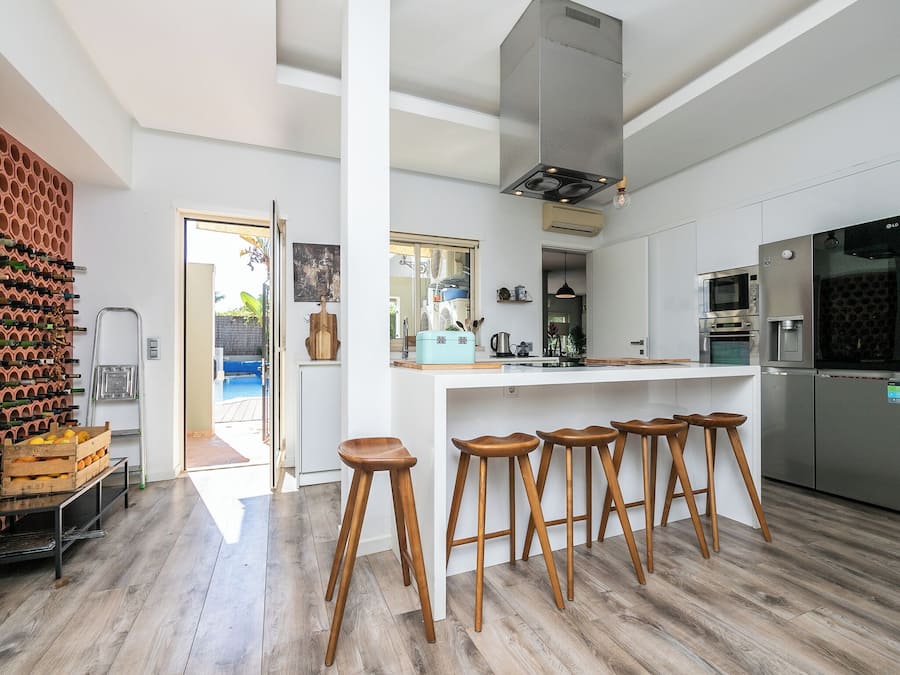 A modern kitchen with a central island, bar stools, stainless steel appliances, and a wine rack.