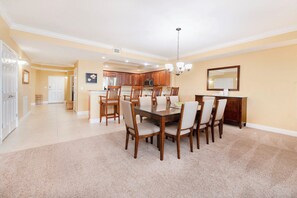 A spacious dining area with a large wooden table and chairs, a kitchen in the background, and a chandelier. - #404 St. Maarten 3/3 Luxury Oceanfront Condo Daytona Beach Shores (Daytona Beach Shores)