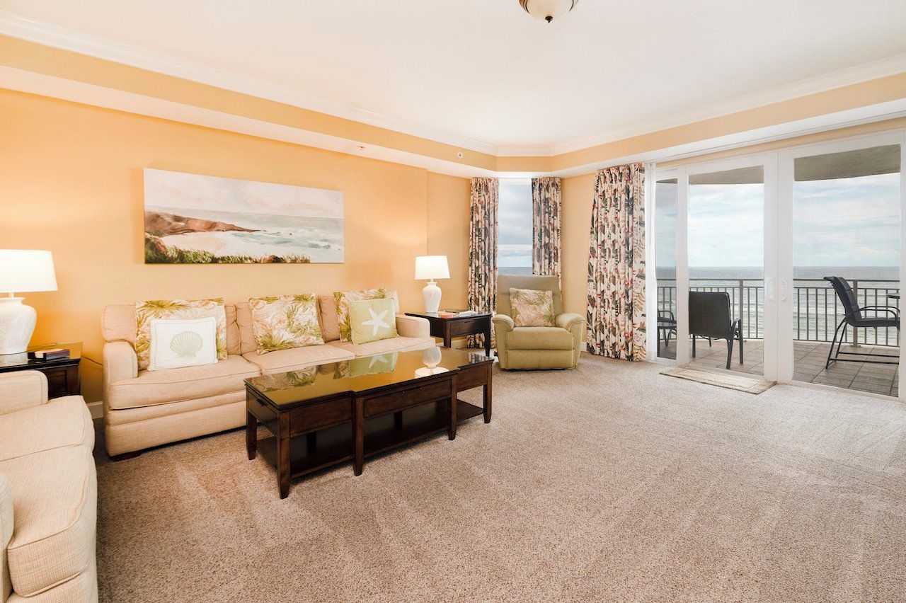 A hotel room with a sofa, armchairs, a coffee table, and a balcony with a view.