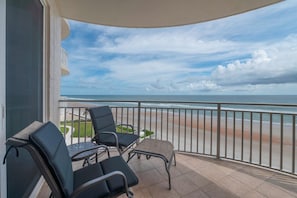 A balcony with two chairs and a small table, overlooking a beach with a clear sky. - #404 St. Maarten 3/3 Luxury Oceanfront Condo Daytona Beach Shores (Daytona Beach Shores)