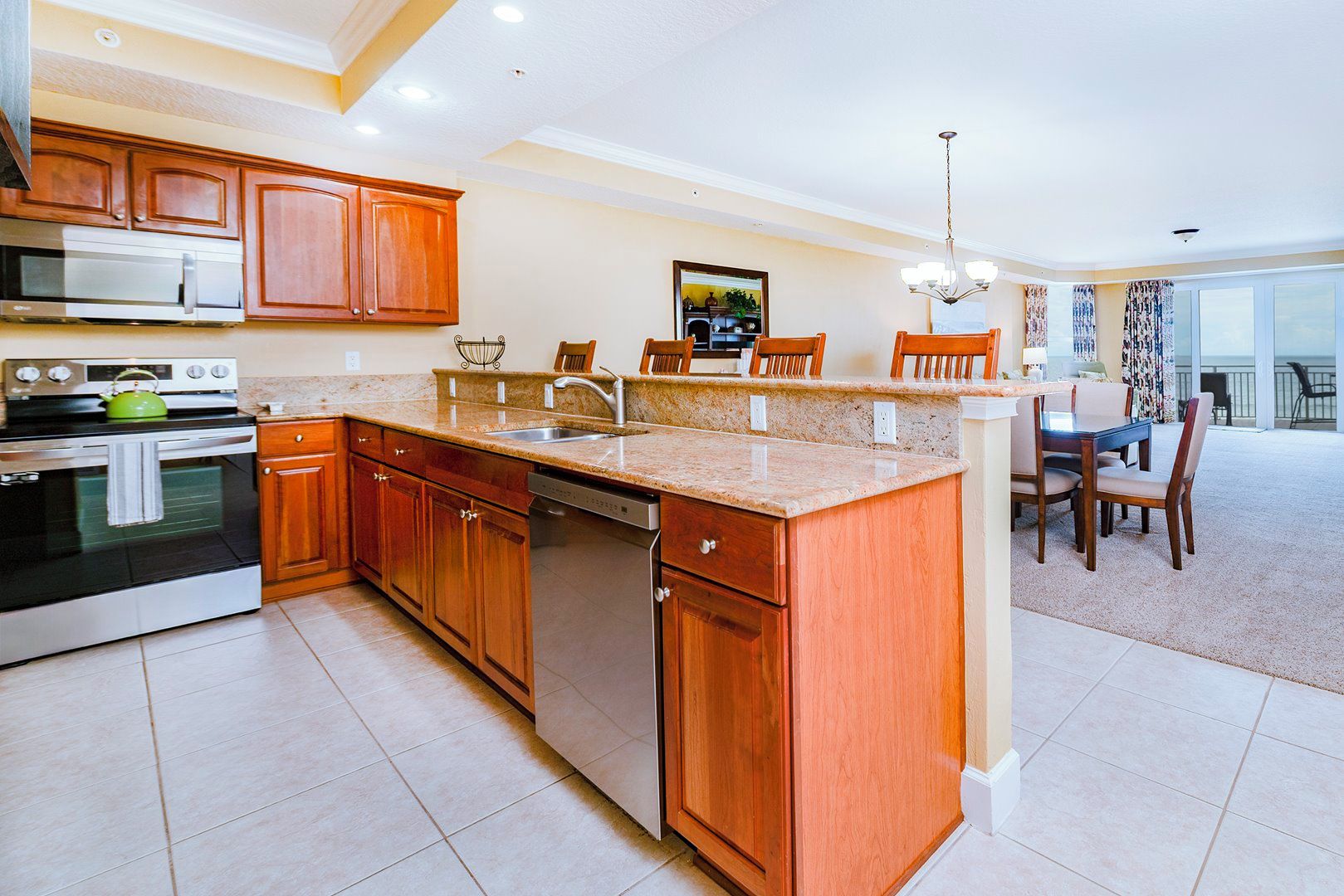 A modern kitchen with wooden cabinets, a built-in oven, and a dishwasher. There is a dining area with a table and chairs.