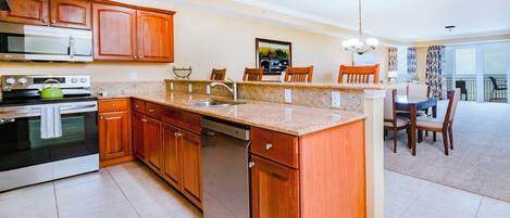 A modern kitchen with wooden cabinets, a built-in oven, and a dishwasher. There is a dining area with a table and chairs.