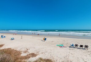 Ein Strand mit blauem Himmel, ruhiger Wellen und mehreren Liegestühlen und Sonnenschirmen.