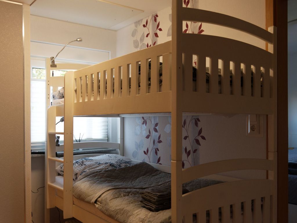 A bunk bed with a window above it, a desk with a lamp, and a wall with a leaf pattern.
