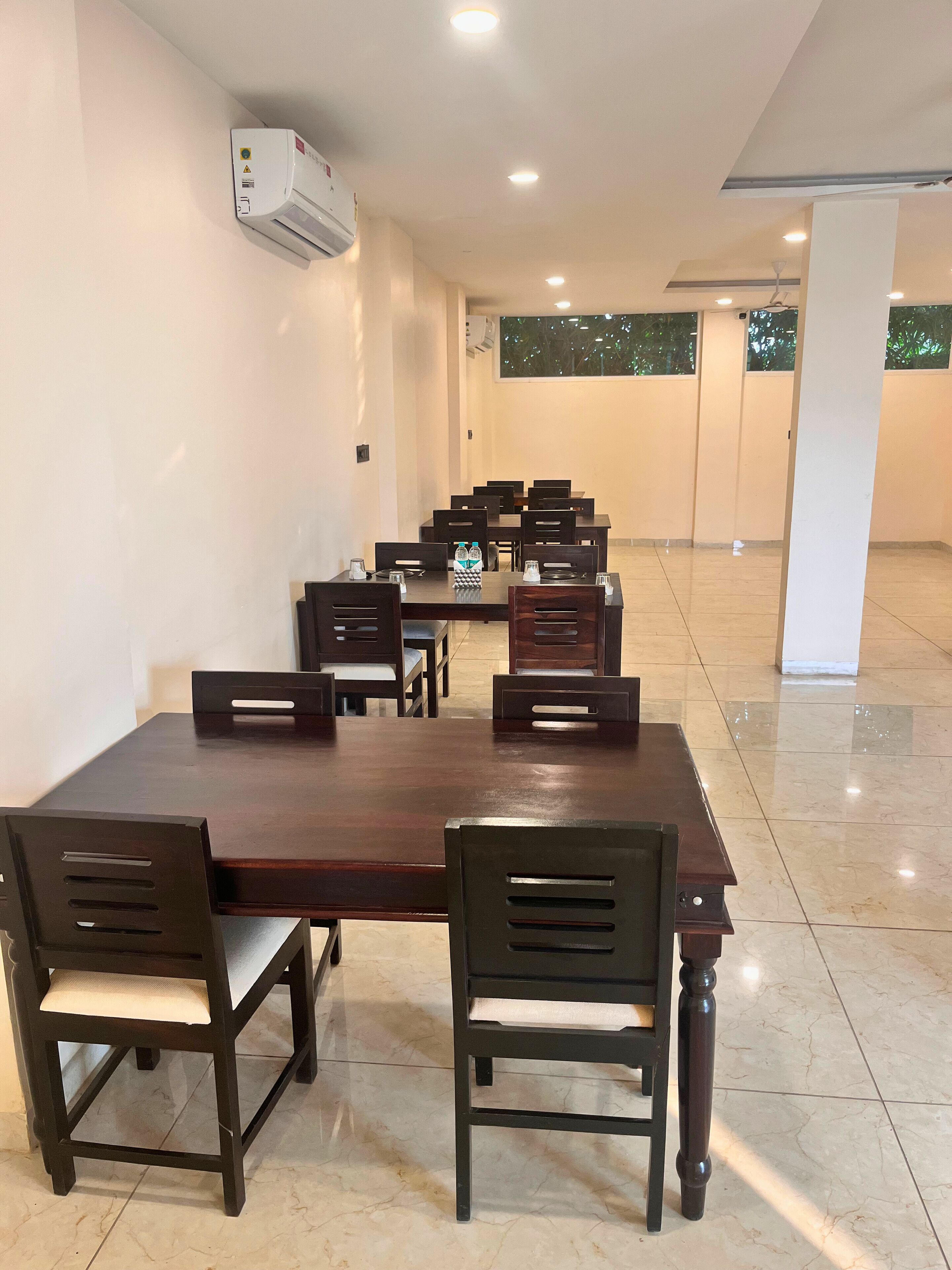 A conference room with a long table and chairs, an air conditioning unit on the wall, and a window with a view of trees.