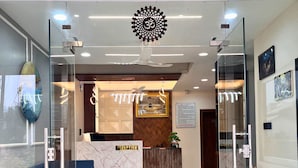 A reception area with a reception desk, a blue sofa, a glass wall, and a ceiling fan. - Hotel Benchmark Prime (Indore)
