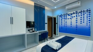 A modern hotel room with a bed, a desk, and a large window with a blue abstract design. - Hotel Benchmark Prime (Indore)