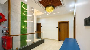 A modern hotel lobby with a glass railing, a blue reception desk, a wooden door, and a chandelier. - Hotel Benchmark Prime (Indore)