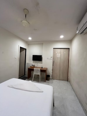 A hotel room with a bed, a desk with a chair, a television, and a wardrobe. - Red House Hostels (Mumbai)