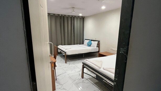 Une chambre d’hôtel avec deux lits, un ventilateur de plafond et une salle de bain visible à travers une porte ouverte.