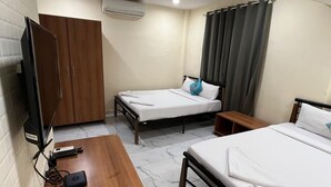 Une chambre d’hôtel avec deux lits simples, un bureau en bois, une télévision et un appareil de climatisation.