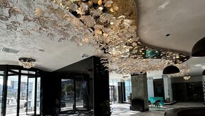 En rymlig entréhall med ett marmorgolv, stora glasdörrar och ett tak med hängande, dekorativa element.