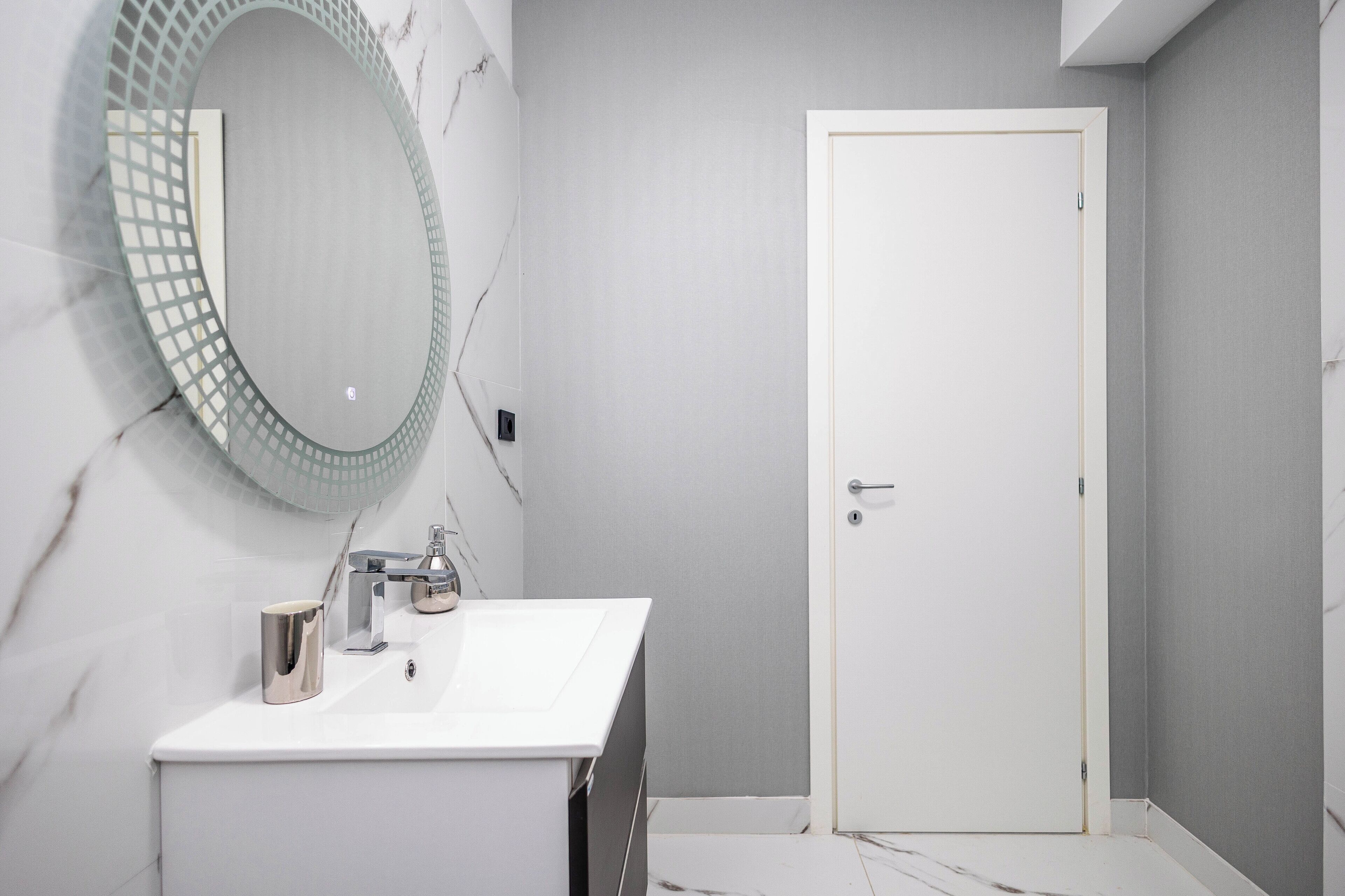 Un bagno con un lavandino bianco, uno specchio con cornice geometrica e una porta con maniglia.