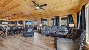 Ein großzügiger Wohnbereich mit Holzboden, Deckenventilator, grauem Sofa, grauem Sessel und Essbereich mit Tisch und Stühlen.