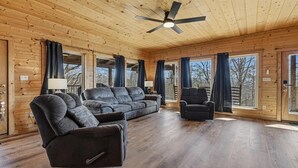Ein rustikales Blockhaus-Interieur mit einer großen Couch, zwei Sesseln und einem Deckenventilator.