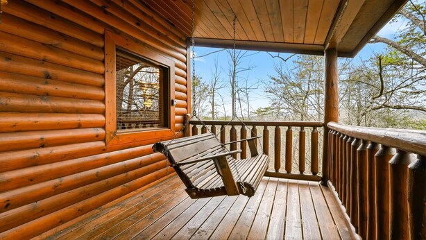 Una cabaña de madera con un porche, un banco y una ventana que da a los árboles.