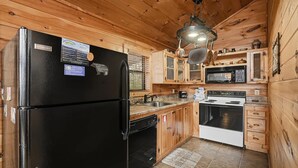 Una cocina compacta con armarios de madera, un refrigerador negro, un microondas, una estufa y un lavamanos.