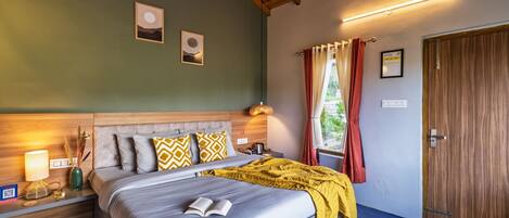 A bedroom with a bed, bedside lamps, a wooden headboard, and a window with curtains.