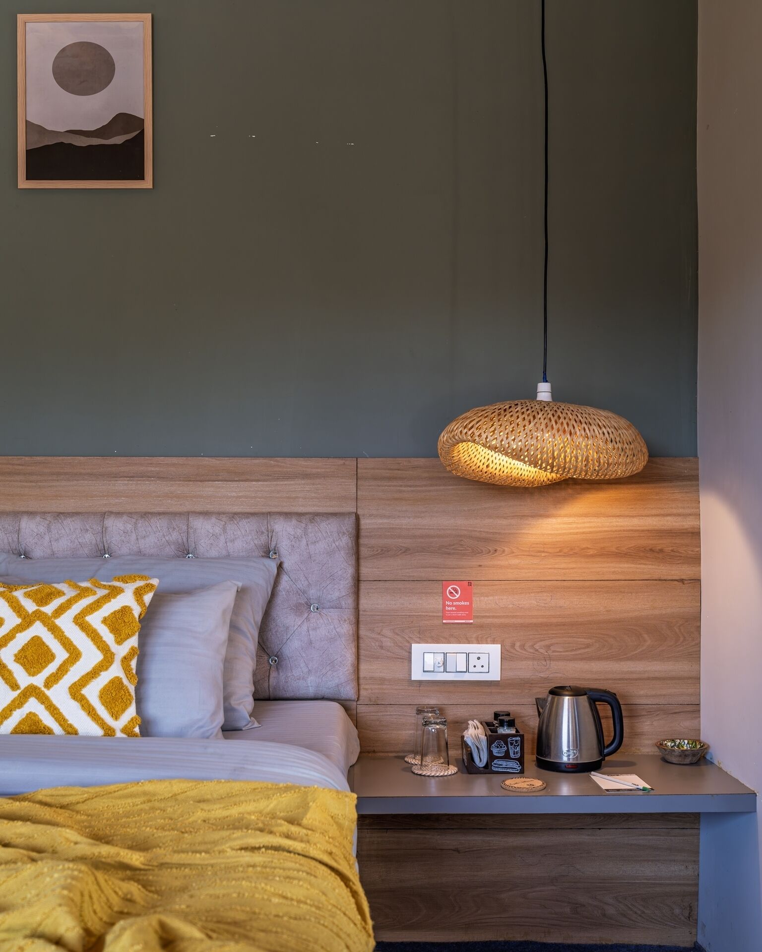A modern hotel room with a bed, a bedside table with a lamp, a coffee maker, and a "No smoking" sign.