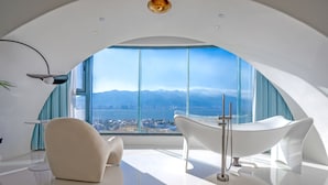Una habitación moderna y espaciosa con un amplio ventanal panorámico, una bañera blanca y un techo elegante y curvo.