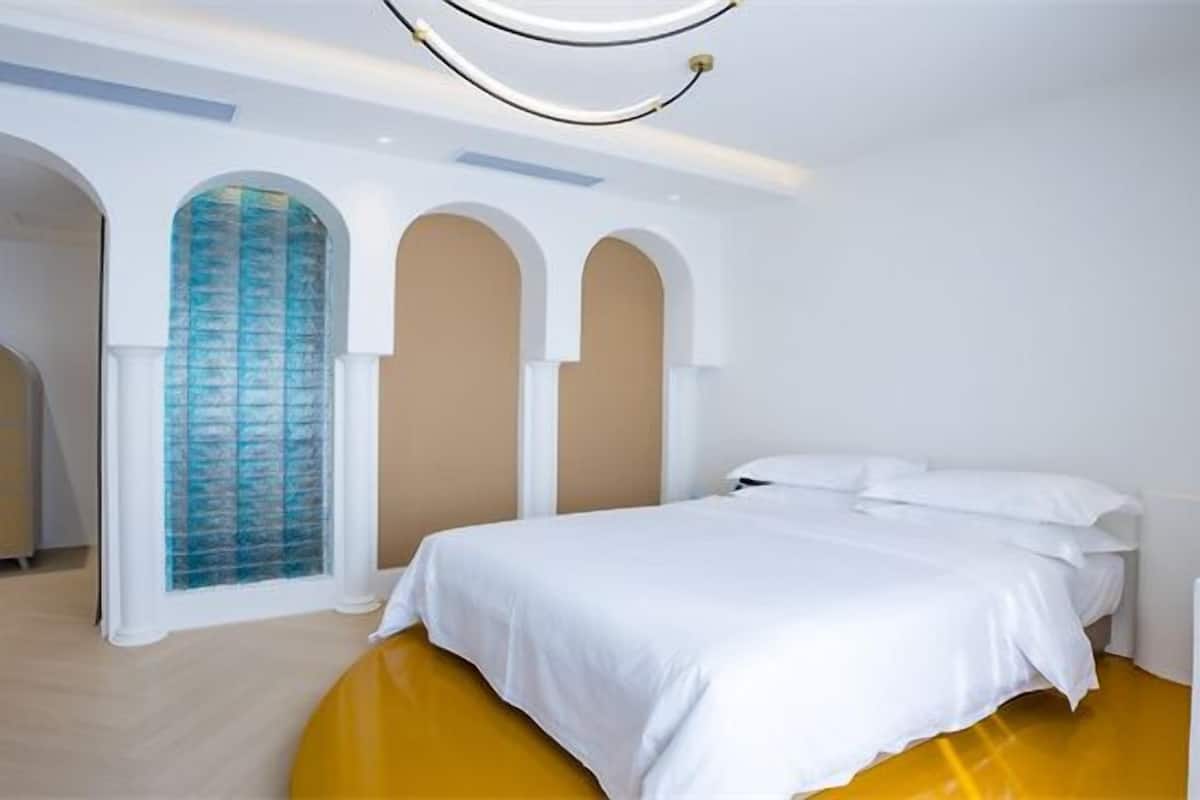 Una habitación de hotel moderna con una cama grande, un área de estar circular y un diseño de ventana en arco único.