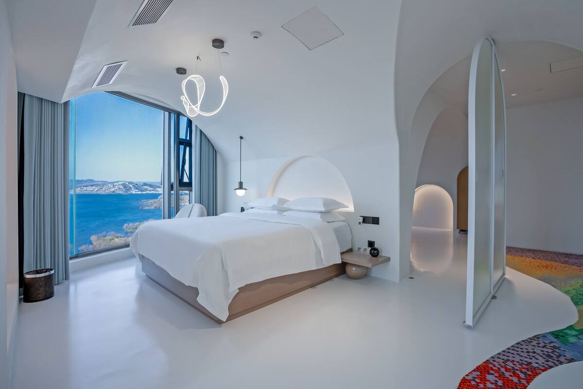 Un dormitorio moderno con una cama grande, vistas al mar y un diseño arquitectónico único.