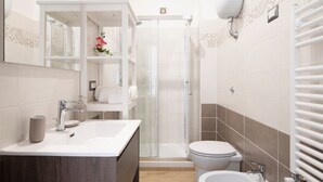Et moderne badeværelse med brusekabine i glas, toilet, håndvask og spejl.