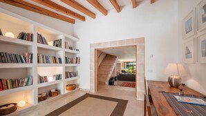 A spacious room with a wooden dining table, a bookshelf filled with books, and a staircase leading to another area. - Villa 'Can Perot' with Mountain View, Private Pool and Wi-Fi (Pollença)