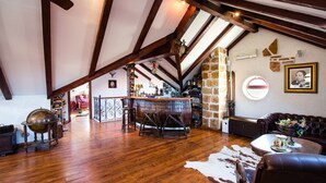 Ein geräumiges Loft mit freiliegenden Holzbalken, einer rustikalen Steinwand, einer Bar mit Hockern und einem Ledersofa.