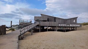 Un bâtiment en bois, sur une plage de sable, avec une pancarte indiquant « HAVEN VAN RENESSE ». Une passerelle en bois mène à ce bâtiment.