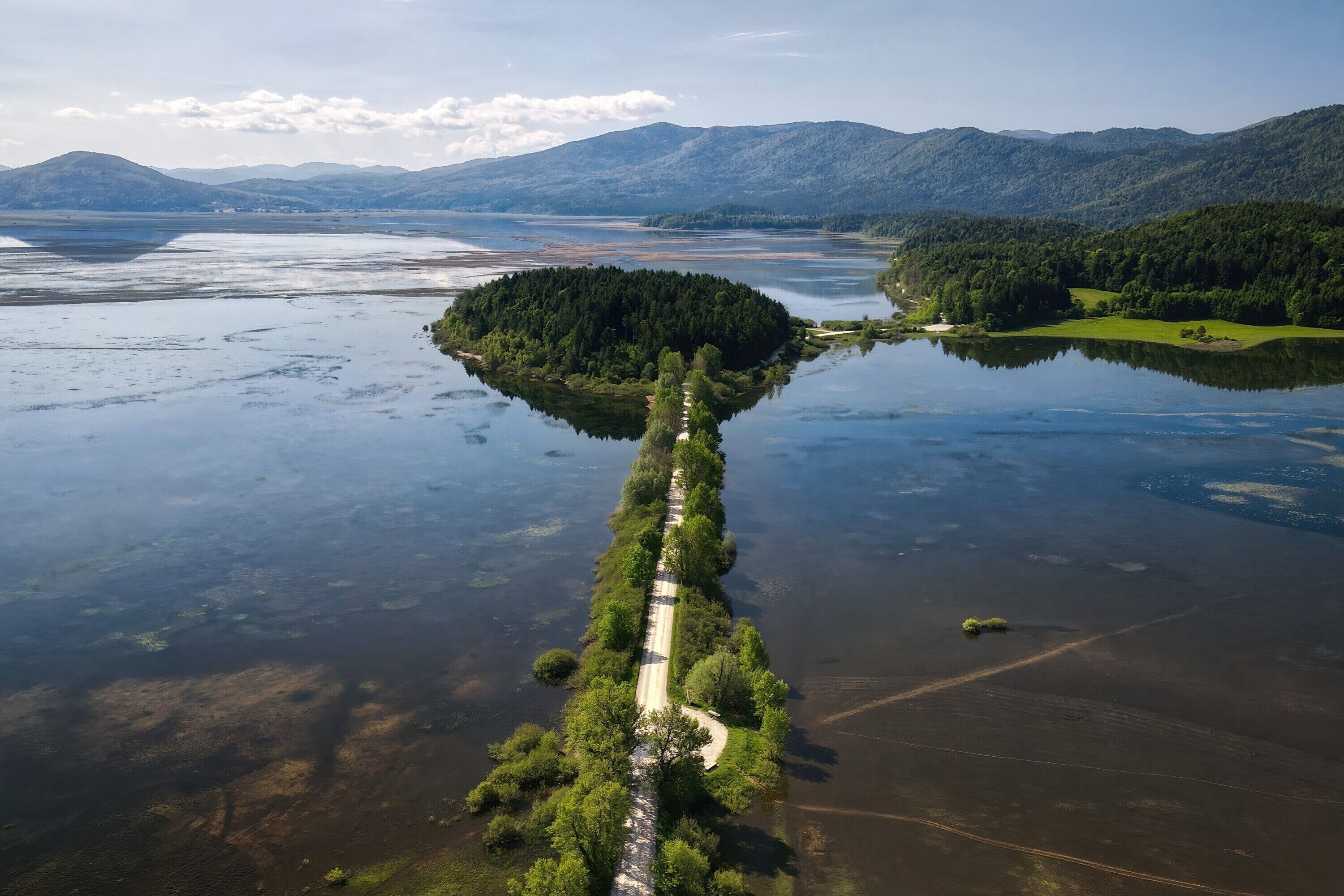 An aerial view of a lake with a narrow, tree-lined path leading to a small island.