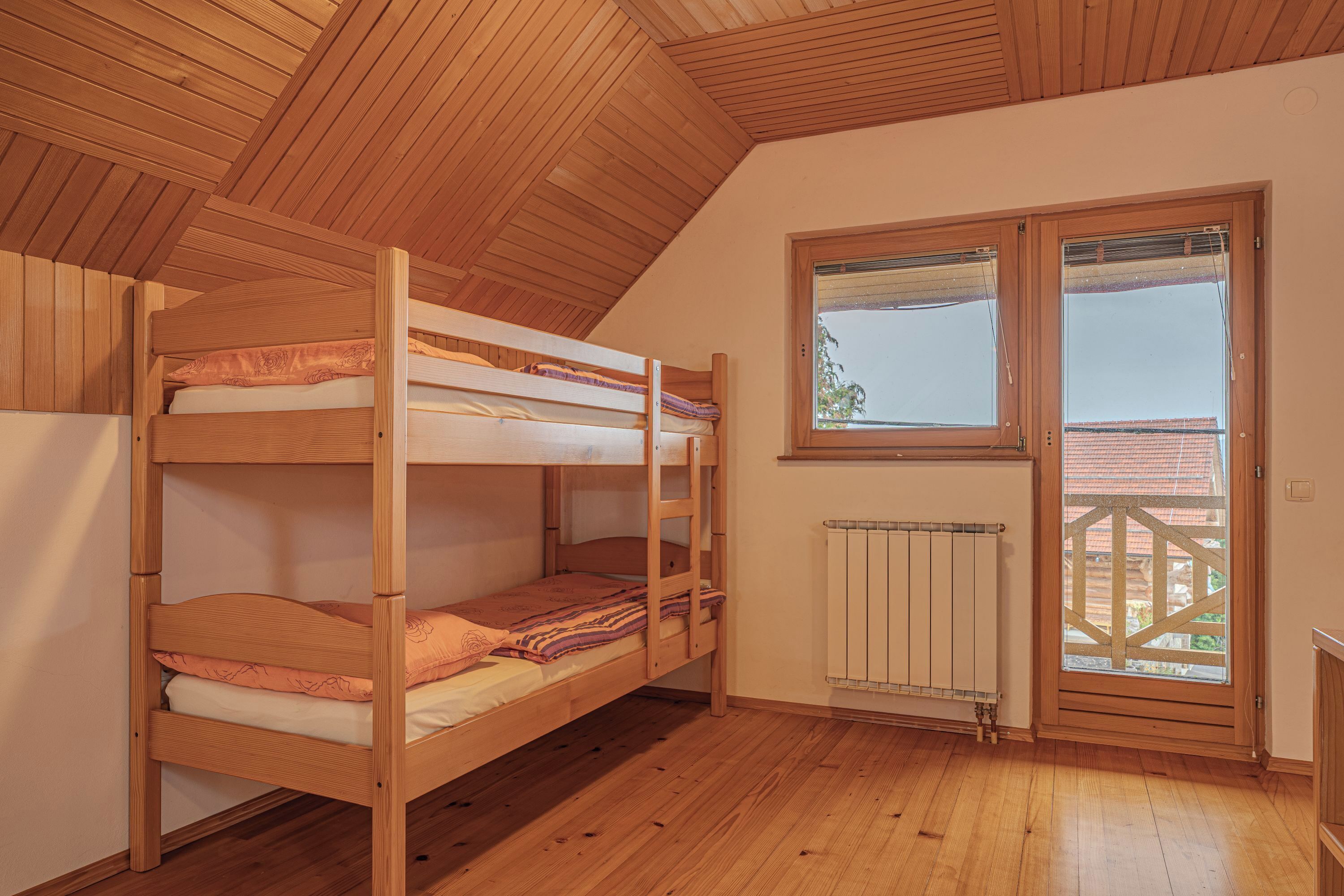 A room with a bunk bed, wooden flooring, a radiator, and a window with a view.