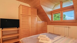 A bedroom with a TV, wooden wardrobe, a bed with a striped bedspread, and a skylight.