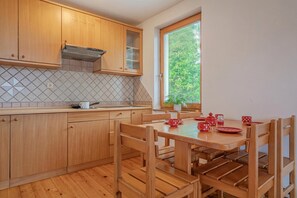 A kitchen with wooden cabinets, a tiled backsplash, a window with blinds, and a dining table with chairs. - Oblak Estate (Ribnica)